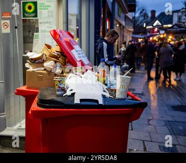 Überfüllte Mülltonnen mit Essensbehältern und Getränken, die auf einer belebten Straße der Stadt entsorgt wurden, als die Leute abends vorbeilaufen York UK 30. November 2024 Stockfoto