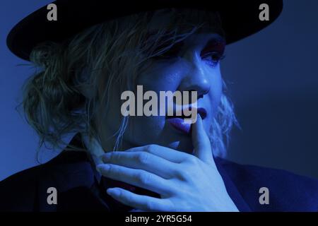 Nahaufnahme einer Frau mit Hut und nachdenklichem Ausdruck unter blauer Beleuchtung, Fotoshooting Stockfoto
