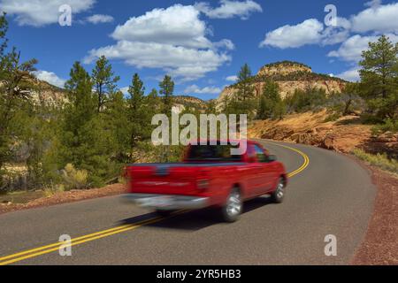 Ein roter Pickup-Truck fährt auf einer gewundenen Straße durch eine malerische Bergregion mit Bäumen und blauem Himmel, Zion-Nationalpark, Utah, USA, Nordamerika Stockfoto