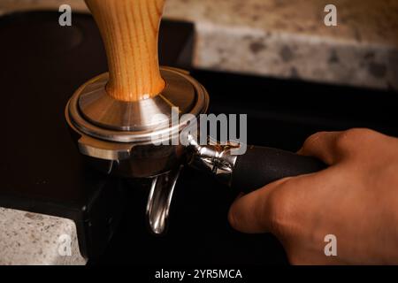 Nahaufnahme eines manuellen Café-Barista, der Kaffee durch manuelles Drücken des gemahlenen Kaffees mit einem Manipulator in einem Café zubereitet. Auf einer speziellen Oberfläche. Stockfoto