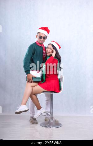 Asiatisches Porträt-Paar mit Partykleidung und Weihnachtsmützen, die Weihnachten und Neujahr feiern, mit 2 Geschenkboxen, die als Zeichen der Liebe lächeln. isola Stockfoto