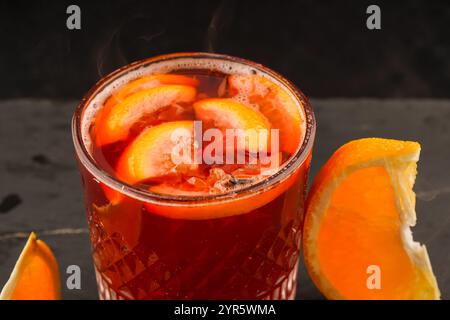 Ein Glas Herbstglühwein. Ein würziges alkoholisches Getränk aus Rotwein, Orange, Zimt, Nelken, Preiselbeeren und Preiselbeeren. Schwarzer Holztisch Stockfoto