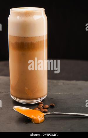 Eine große Tasse Kaffee. Daneben liegt ein Löffel tropfender Honig und Kaffeebohnen. Gute Fotoqualität. Auf schwarzem Hintergrund. Stockfoto