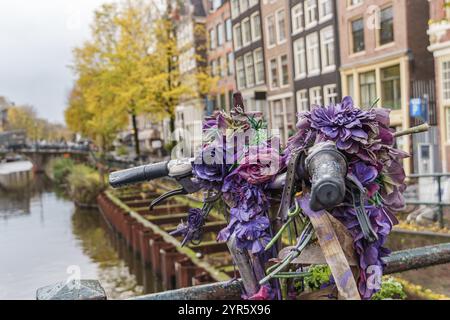 Dekoriertes Fahrrad mit lila Blumen auf einer Brücke in einer städtischen Umgebung, Amsterdam, Niederlande Stockfoto