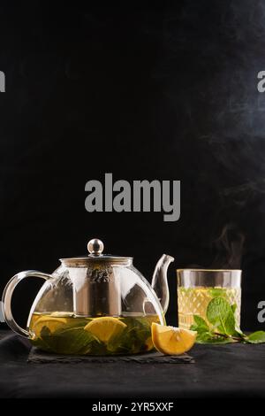 Glas-Teekanne mit heißem Zitrustee aus Orangen, Zitronen und Limetten, gesundes Getränk auf dunklem Hintergrund. Stockfoto