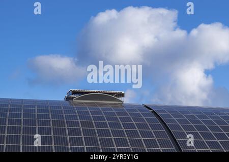 Gekrümmte Solarpaneele, die auf einem Dach installiert sind, erzeugen unter einem bewölkten blauen Himmel saubere Energie und zeigen nachhaltige Energiepraktiken Stockfoto