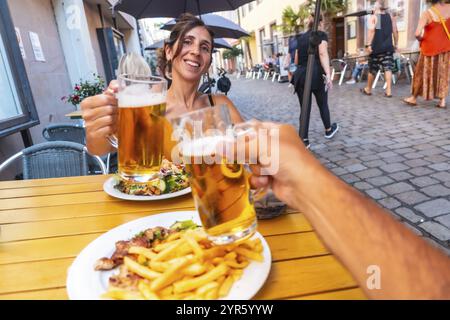 Ein Mann und eine Frau halten ihre Biergläser in einem Restaurant hoch. Die Frau lächelt und der Mann lächelt zurück. Die Atmosphäre ist freundlich und Re Stockfoto
