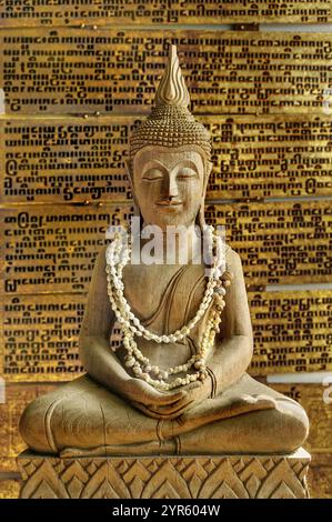 Hölzerner Thai-Buddha mit Muschelketten vor einem Pali-Buch aus Myanmar, Souvenir in Deutschland Stockfoto