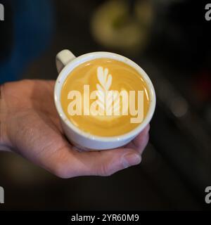 Barista hält einen frisch gebrauten Latte mit Leaf Latte Art Stockfoto