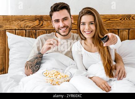 Unterhaltung am Abend. Lächelnder Mann isst Popcorn, Frau drückt Knopf auf der Fernbedienung Stockfoto