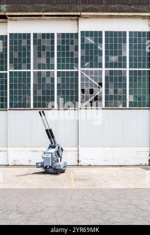 Eine große, altmodische Waffe sitzt auf einem Parkplatz neben einem Gebäude. Die Waffe ist eine Waffe aus dem Zweiten Weltkrieg, und sie ist von einer Menge Empt umgeben Stockfoto