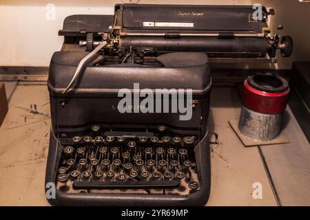 Eine alte Schreibmaschine sitzt auf einem Tisch. Die Schreibmaschine ist schwarz und hat einen silbernen Griff. Die Schreibmaschine ist von der Firma L.S.M Stockfoto