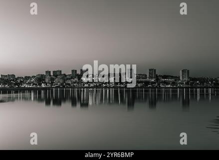 Die Lichter der Stadt spiegeln sich auf dem Fluss douro mit der Skyline von porto im Hintergrund in der Abenddämmerung und schaffen eine friedliche und faszinierende Stadtlandschaft in Schwarz und W Stockfoto