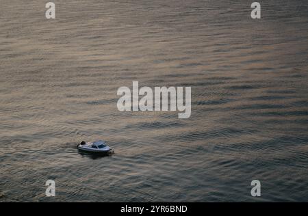 Ein kleines Motorboot segelt friedlich auf einem ruhigen Meer bei Sonnenuntergang und erzeugt entspannende Wellen im Wasser. Die Szene ist ruhig und beschaulich, beschwört Frieden und Stockfoto