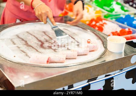 Frau, die frittierte Eisbrötchen in der Gefrierpfanne auf dem Street Food Market. Handgefertigtes Rolleis Dessert. Stockfoto