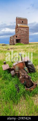 Ein alter Traktor sitzt auf einem Feld neben einem Getreidesilo. Der Traktor ist verrostet und alt, und auch das Silo ist alt und verlassen. Das Konzept der Nostalgie Stockfoto