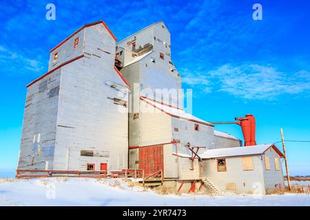 Ein großes, altes Getreidesilo ist von Schnee umgeben. Das Gebäude befindet sich in einer ländlichen Gegend und er ist verlassen. Der Himmel ist klar und blau, und der schneebedeckte gr Stockfoto