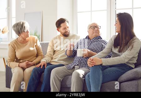 Familie älterer alter Eltern und ihrer erwachsenen Kinder sitzen zu Hause und unterhalten sich mit einer Tasse Tee Stockfoto