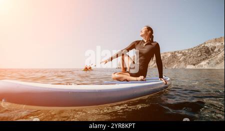 Frau Paddleboarding Ocean Sunset - Eine Frau sitzt auf einem Paddleboard im Meer bei Sonnenuntergang. Stockfoto