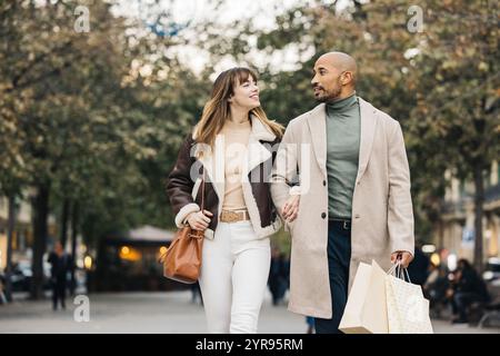 Ein glückliches Paar spaziert Arm in Arm durch eine Stadtstraße und genießt einen gemeinsamen Einkaufstag. Stockfoto