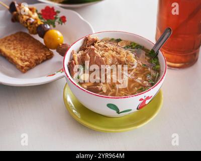 Soto Kudus ist ein typisches Kudus-Essen, das einer Suppe ähnelt, die Büffelfleisch enthält, serviert mit Tempeh Satay und Hühnerabfällen und einem Glas Tee Stockfoto