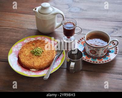 Kunafa oder Kunefe ist ein traditionelles Dessert aus dem Nahen Osten. Serviert mit türkischem Kaffee und gewürztem Kaffee auf einem Holztisch Stockfoto