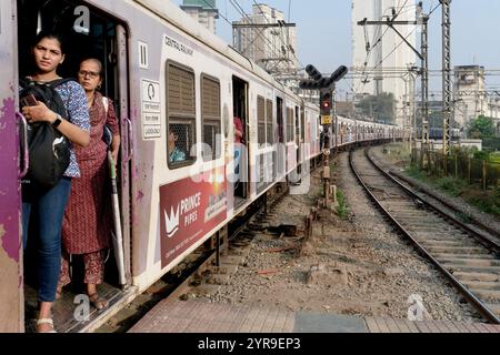 Mumbai, Indien: Weibliche Passagiere stehen prekär an der offenen Tür eines Vorortzuges, der in den Chhatrapati Shivaji Maharaj Terminus fährt Stockfoto