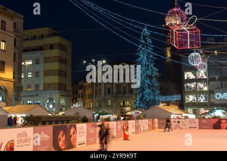 Eislaufbahn in der Stadt während der Weihnachtszeit am Abend, mit weihnachtsmarkt, farbigen Lichtern und einem großen Weihnachtsbaum. Varese, Italien Stockfoto