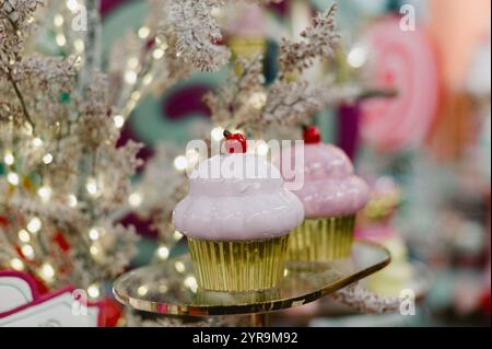 Zwei Cupcakes stehen auf einem Tisch. Einer ist rosa und der andere weiß. Auf dem rosa Cupcake ist eine Kirsche drauf Stockfoto