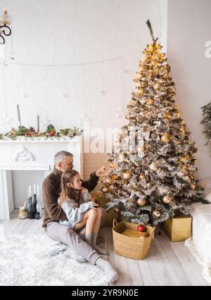 Vater und Tochter schmücken einen Weihnachtsbaum. Gemütliche und herzzerreißende Familienszene. Stockfoto