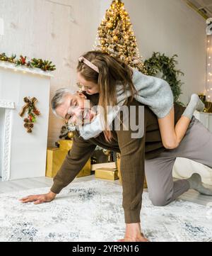 Der Vater reitet seiner Tochter in festlicher Weihnachtsstimmung mit dem Huckepack. Fröhlicher Familienmoment. Stockfoto
