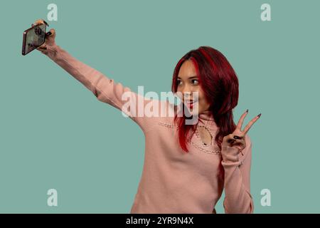 Fröhlicher Influencer macht ein Selfie mit Smartphone und macht ein Friedenszeichen Stockfoto