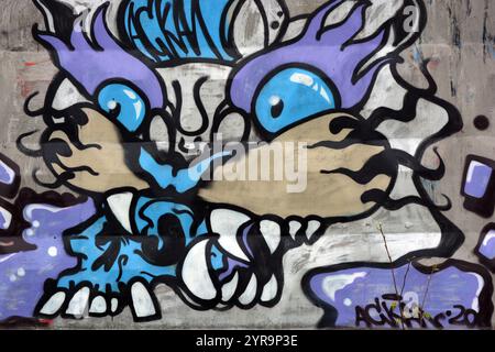 Graffiti, Inschrift, Zeichnung des Kopfes einer bösen Katze, eines Tigers von blau, lila, weiß, pfirsichfarben mit großen weißen Zähnen, schwarzen Barthaaren. Stockfoto