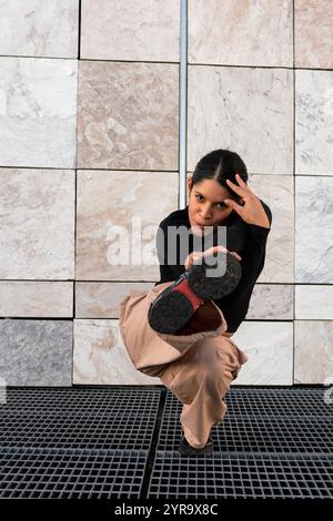 Eine junge Frau in braunen Hosen und schwarzem T-Shirt Breakdance, die auf einem Metallgitter posiert. Sportlichkeit und Geschicklichkeit, wie es die Frau kann Stockfoto