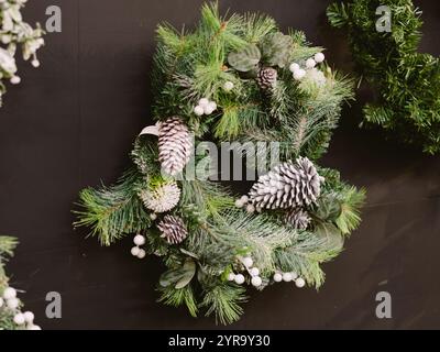 Ein wunderschöner Kranz aus Tannenzapfen und weißen Beeren hängt an einer Wand. Die Tannenzapfen sind in der Mitte des Kranzes angeordnet, wobei sich einige davon überlappen Stockfoto