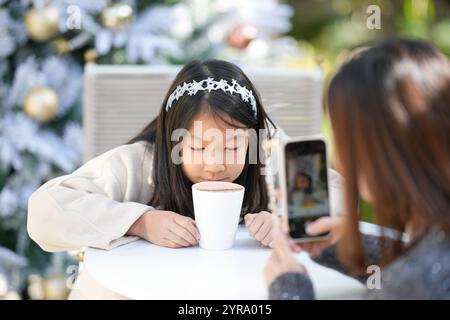 Eine singapurische Frau im Alter von 40 Jahren spricht mit ihrem Smartphone in einem hübschen Café mit Weihnachtsmotiven im Zentrum von Shanghai, China, und fotografiert ihre 9-jährige Stockfoto