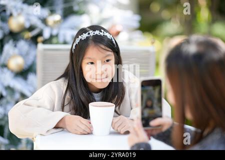 Eine singapurische Frau im Alter von 40 Jahren spricht mit ihrem Smartphone in einem hübschen Café mit Weihnachtsmotiven im Zentrum von Shanghai, China, und fotografiert ihre 9-jährige Stockfoto