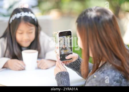 Eine singapurische Frau im Alter von 40 Jahren spricht mit ihrem Smartphone in einem hübschen Café mit Weihnachtsmotiven im Zentrum von Shanghai, China, und fotografiert ihre 9-jährige Stockfoto