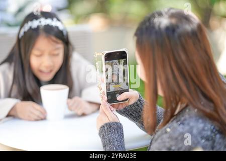 Eine singapurische Frau im Alter von 40 Jahren spricht mit ihrem Smartphone in einem hübschen Café mit Weihnachtsmotiven im Zentrum von Shanghai, China, und fotografiert ihre 9-jährige Stockfoto