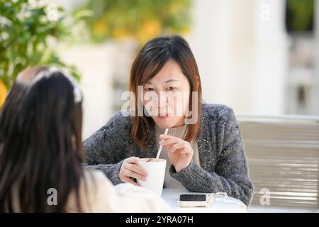 Eine singapurische Frau im Alter von 40 trinkt heiße Schokolade, während sie mit ihrer 9-jährigen Tochter in einem hübschen Weihnachtscafé in der Innenstadt von Shan spricht Stockfoto