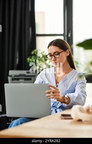 Eine schöne junge Frau in Brille arbeitet intensiv an ihrem Laptop in einer stilvollen Büroumgebung. Stockfoto