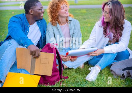 Gruppe verschiedener Schüler, die auf Gras sitzen und lächeln, während sie Notizbücher halten Stockfoto