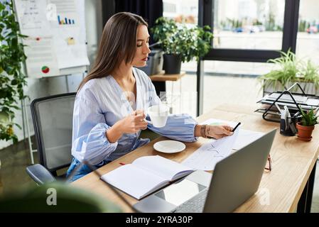 Brünette arbeitet intensiv in einem hellen, mit Pflanzen gefüllten Büro mit Kaffee in der Hand. Stockfoto