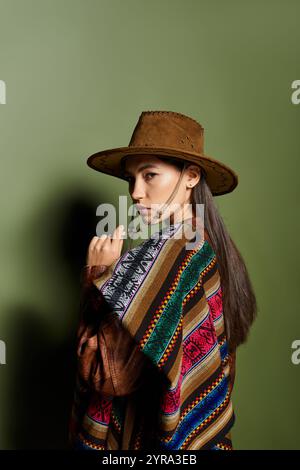 Die junge Frau posiert anmutig und zeigt ihren leuchtenden Poncho vor einem üppigen grünen Hintergrund. Stockfoto