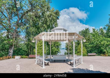 Malerischer weißer Pavillon auf dem Platz im Sommerpark, Strukovsky Garden, Samara, Russland. Bänke, eingerahmt von üppigem Grün, Blick auf den Fluss Wolga. Ruhig Stockfoto