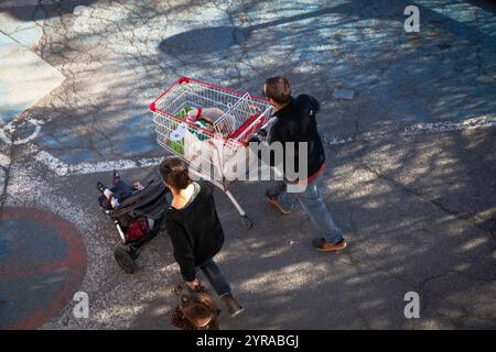 Ein Paar mit einem Kind verlässt einen Supermarkt mit einem Einkaufswagen voller Lebensmittel *** örtlicher Titel *** Stockfoto