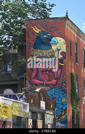 Kanada, Quebec, Montreal: Street Art. Fresko einer Frau, die eine gehörnte Tiermaske trägt, von der Künstlerin SBU One auf einem Gebäude mit roten Ziegelwänden als Teil von t Stockfoto