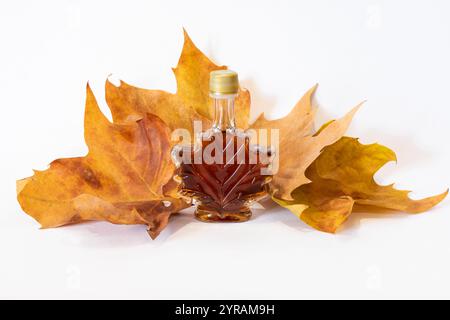 Ahornblatt Form Flasche mit Ahornblatt Sirup mit Ahornblatt Herbstblatt's auf weißem Hintergrund. Organischer reiner Sirup. Sirup in Glasflasche. Dekoratives Glas Stockfoto