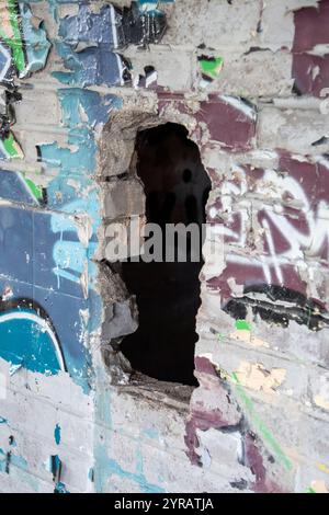 Yorkshire, Großbritannien: 31. Mai 2024 – Ein Loch in der Graffiti-bedeckten Wand des vernachlässigten Castle College Sportplatzes Umkleideraum Stockfoto