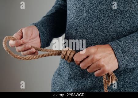 Nahaufnahme eines Mannes, der ein Juteseil mit einer Schlinge vor grauem Hintergrund hält Stockfoto